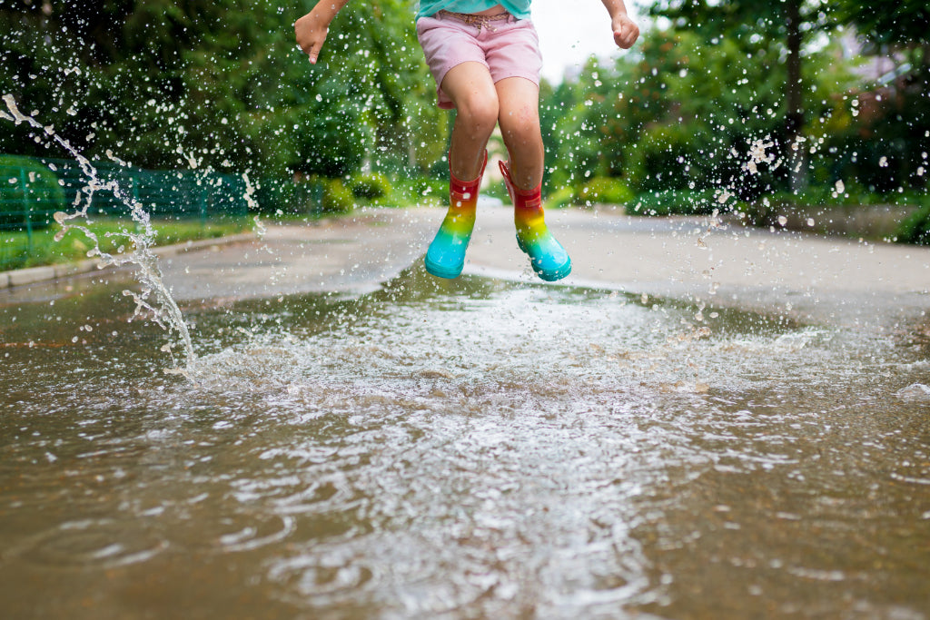 Child jumps in puddle wearing boots